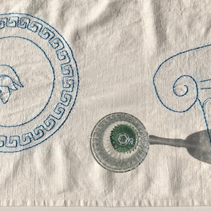 Hand-embroidered mediterranean table runner with an ancient Greek theme featuring a statue, column, plate, lyre, eye, olive branch, grapes