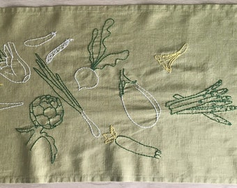 Hand-embroider table runner green linen with spring vegetables, baguette, olive oil cruet, cutlery, salt and pepper shaker