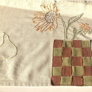 Hand-embroider beige linen table runner with a sunflower, vase brown-green checkers, tin of sardines, baguettes, oyster, olives, pear
