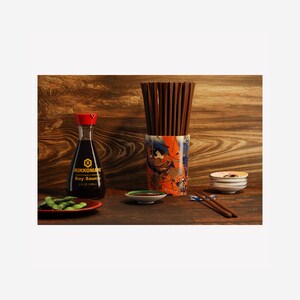 Könnte beinhalten: Ein Holztisch mit einer Flasche Kikkoman Sojasauce, einer kleinen Schale Sojasauce, einem Teller Edamame, einem Stäbchenhalter mit Stäbchen und einem Stapel kleiner Teller.