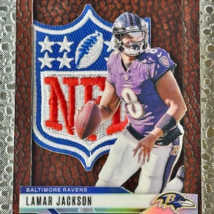 May include: A football trading card featuring Lamar Jackson of the Baltimore Ravens. The card has a brown textured border and includes the NFL logo in blue, white, and red. Jackson is in a purple jersey, holding a football.