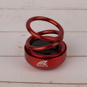 May include: Red car air freshener with a spring-like design and the logo "Motozoom" printed on the bottom.