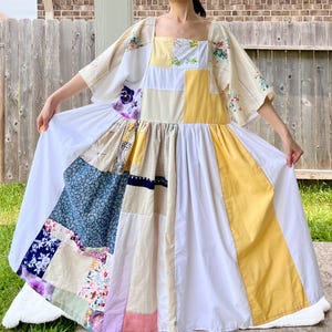 May include: A patchwork dress with a square neckline and short sleeves. The dress incorporates diverse fabric patterns, including floral, solid yellow, and white panels. The skirt is long and flowing, with a mix of colours and textures.