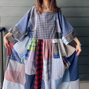 May include: A patchwork dress in a variety of plaid patterns, including blue, red, grey, and white. The dress has a square neckline and wide sleeves. The skirt is a patchwork of different plaid fabrics.