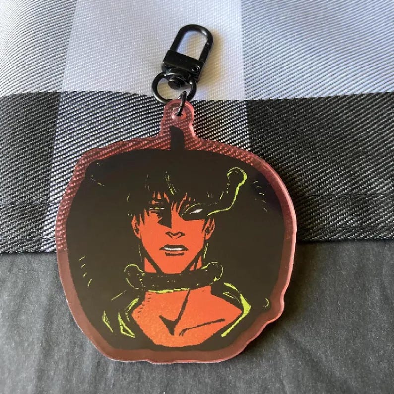 May include: A red and black anime character keychain with a green snake design. The character has a red face and black hair.