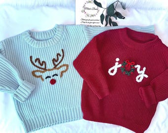 May include: Two children's sweaters. One is light blue with a reindeer face design. The other is red with the word "joy" and a wreath design. Both sweaters are knit.