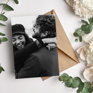 May include: A black and white photo of a couple hugging. The woman is laughing and the man is smiling. They are both wearing casual clothing.