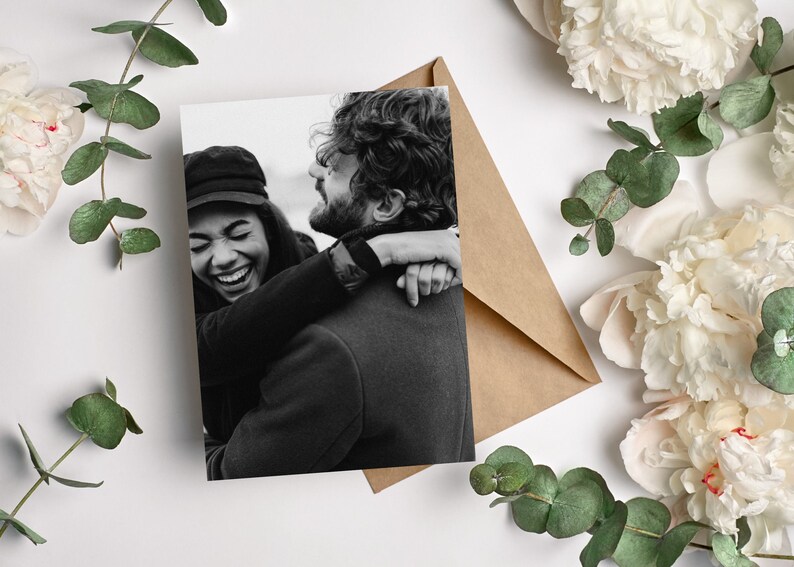 May include: A black and white photo of a couple hugging. The woman is laughing and the man is smiling. They are both wearing casual clothing.