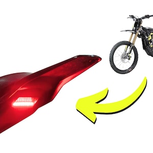 May include: A black electric motorcycle with yellow accents is shown next to a red tail light with a white light. A yellow arrow points from the tail light to the motorcycle. The motorcycle has black tires and a black seat.