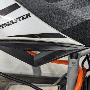 Puede incluir: Primer plano de un simulador de carreras blanco y negro con la palabra "THRUSTMASTER" impresa en el lateral. El simulador tiene un volante negro y gris y un asiento negro y gris.