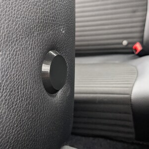 Op de afbeelding: Close-up van een zwarte leren autostoel met een zwarte plastic knop op de hoofdsteun.