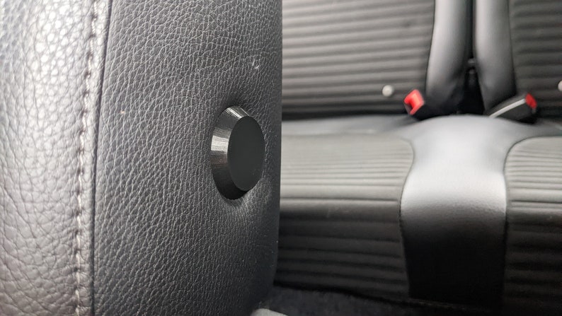 Op de afbeelding: Close-up van een zwarte leren autostoel met een zwarte plastic knop op de hoofdsteun.