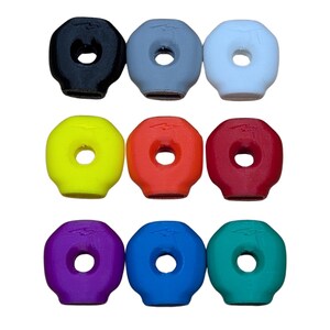 Op de afbeelding: Negen kleurrijke, donutvormige rubberen stoppen in een raster. De stoppen zijn in verschillende kleuren: zwart, grijs, wit, geel, oranje, rood, paars, blauw en teal. Elke stop heeft een centraal gat.