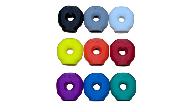Op de afbeelding: Negen kleurrijke, donutvormige rubberen stoppen in een raster. De stoppen zijn in verschillende kleuren: zwart, grijs, wit, geel, oranje, rood, paars, blauw en teal. Elke stop heeft een centraal gat.