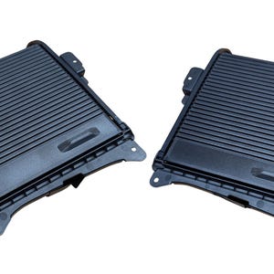 May include: Two black plastic car console storage compartments. Each compartment has a rectangular shape with a ridged top and a small recessed handle. The compartments are designed to fit into a vehicle's interior.