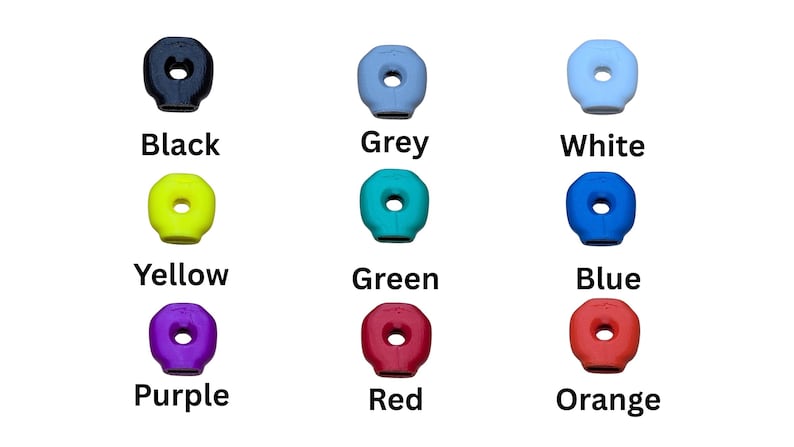 Op de afbeelding: Een verzameling van negen kleurrijke, donutvormige objecten. De kleuren zijn zwart, grijs, wit, geel, groen, blauw, paars, rood en oranje. Elk object heeft een centraal gat en een label met de kleurnaam.