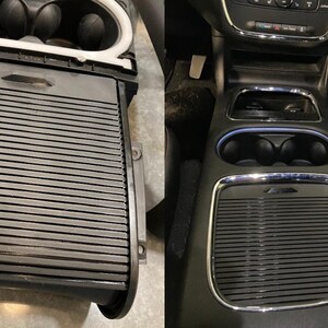 May include: Close-up of a black car interior with a storage compartment and cup holders. The compartment has a black, ribbed lid and the cup holders are made of chrome.