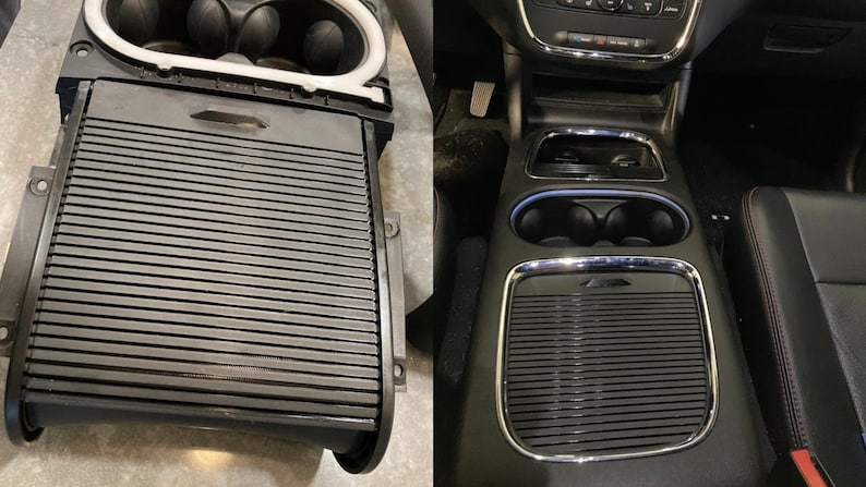 May include: Close-up of a black car interior with a storage compartment and cup holders. The compartment has a black, ribbed lid and the cup holders are made of chrome.