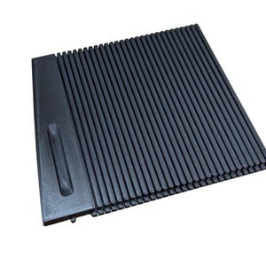 May include: A dark gray, rectangular, ridged object with a smooth, raised section on the left side. The ridges run vertically across the main body of the object. The object is set against a white background.
