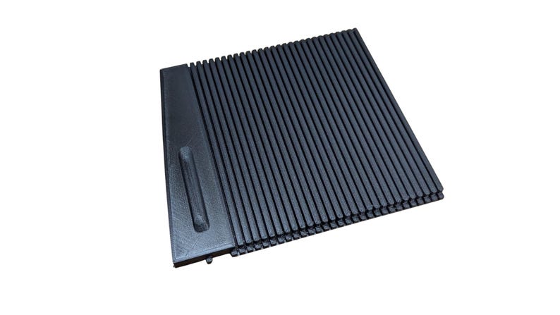 May include: A dark gray, rectangular, ridged object with a smooth, raised section on the left side. The ridges run vertically across the main body of the object. The object is set against a white background.