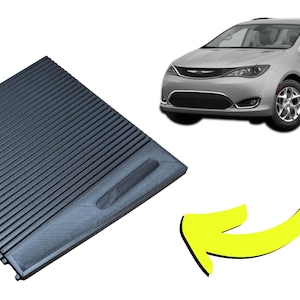 May include: A black, ridged cargo cover, likely for a vehicle, is shown. The cover is rectangular with parallel grooves. A silver minivan is in the background. The text "V2" is also present.