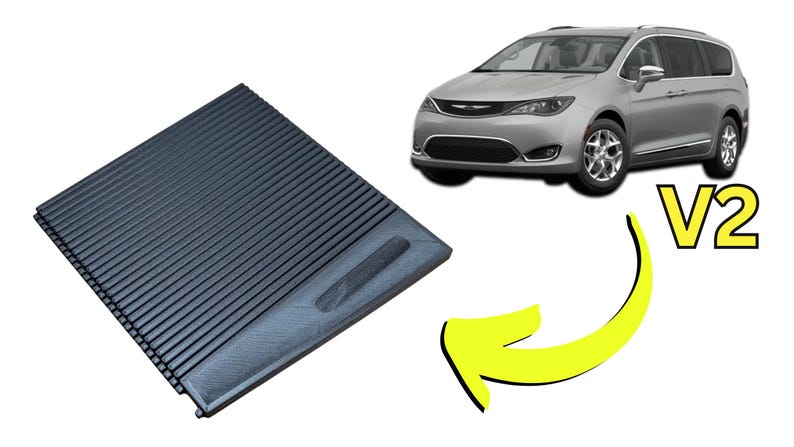 May include: A black, ridged cargo cover, likely for a vehicle, is shown. The cover is rectangular with parallel grooves. A silver minivan is in the background. The text "V2" is also present.