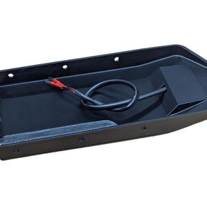 May include: A black, rectangular automotive part with a recessed interior. It features a black wire with red-tipped connectors and several mounting holes. The part is designed for automotive applications.