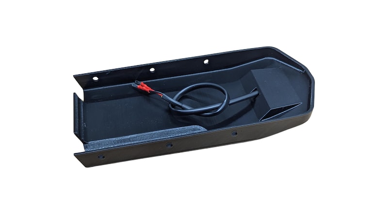 May include: A black, rectangular automotive part with a recessed interior. It features a black wire with red-tipped connectors and several mounting holes. The part is designed for automotive applications.