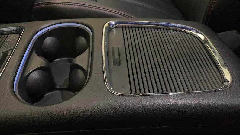 May include: Close-up of a black leather car interior with a chrome-trimmed cup holder and a black, ribbed, rectangular air vent.