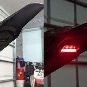 May include: Black motorcycle tail section with integrated LED brake light. The tail section is made of a textured material and has a sleek, aerodynamic design. The LED light glows bright red when illuminated, enhancing visibility.