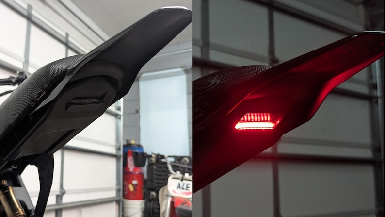 May include: Black motorcycle tail section with integrated LED brake light. The tail section is made of a textured material and has a sleek, aerodynamic design. The LED light glows bright red when illuminated, enhancing visibility.