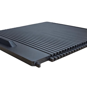 May include: A black plastic car part with a textured surface and a small handle. The part has a series of parallel lines and a grid pattern.