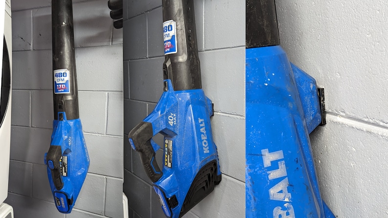 K&ouml;nnte beinhalten: Zwei blaue und schwarze kabellose Laubbl&auml;ser, die an einer Wand h&auml;ngen. Die Gebl&auml;se sind mit "40V MAX" und "KOALT" beschriftet und haben einen Aufkleber mit der Aufschrift "480 CFM 110 MPH".