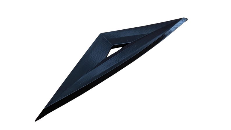 Puede incluir: Un cuchillo de lanzamiento triangular negro con una punta afilada y un borde ligeramente curvo.