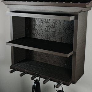 Peut inclure: Un organisateur mural brun fonc&eacute; dot&eacute; d'un sommet en forme de toit, de deux &eacute;tag&egrave;res ouvertes et d'un panneau arri&egrave;re &agrave; motif g&eacute;om&eacute;trique en &eacute;toile. La partie inf&eacute;rieure comprend quatre crochets cylindriques avec deux trousseaux de cl&eacute;s.