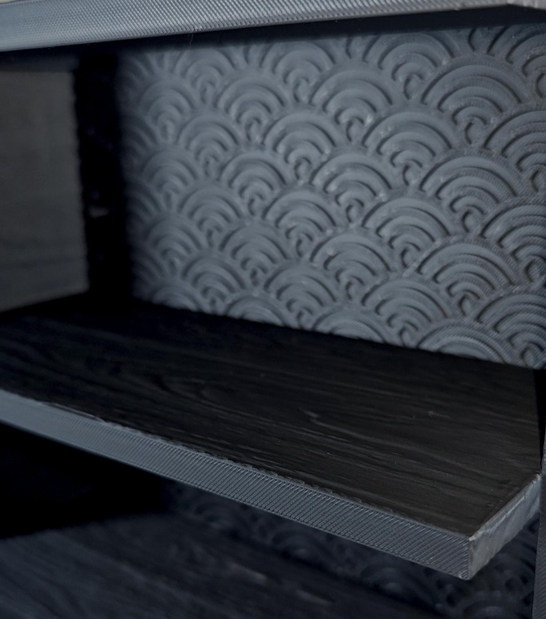 Peut inclure: Une unit&eacute; de rangement gris fonc&eacute; dot&eacute;e d'une &eacute;tag&egrave;re &agrave; texture de grain de bois et d'un panneau arri&egrave;re orn&eacute; d'un motif en relief r&eacute;p&eacute;titif de demi-cercles superpos&eacute;s. La structure est faite d'un mat&eacute;riau gris fonc&eacute; mat avec des couches visibles.