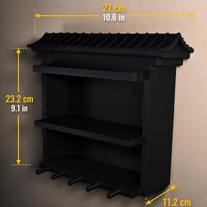 Peut inclure: Une &eacute;tag&egrave;re murale noire &agrave; trois niveaux avec cinq crochets en bas. Le sommet pr&eacute;sente une structure en forme de toit. Les dimensions sont de 27 cm de largeur, 23,2 cm de hauteur et 11,2 cm de profondeur, indiqu&eacute;es par le texte jaune.