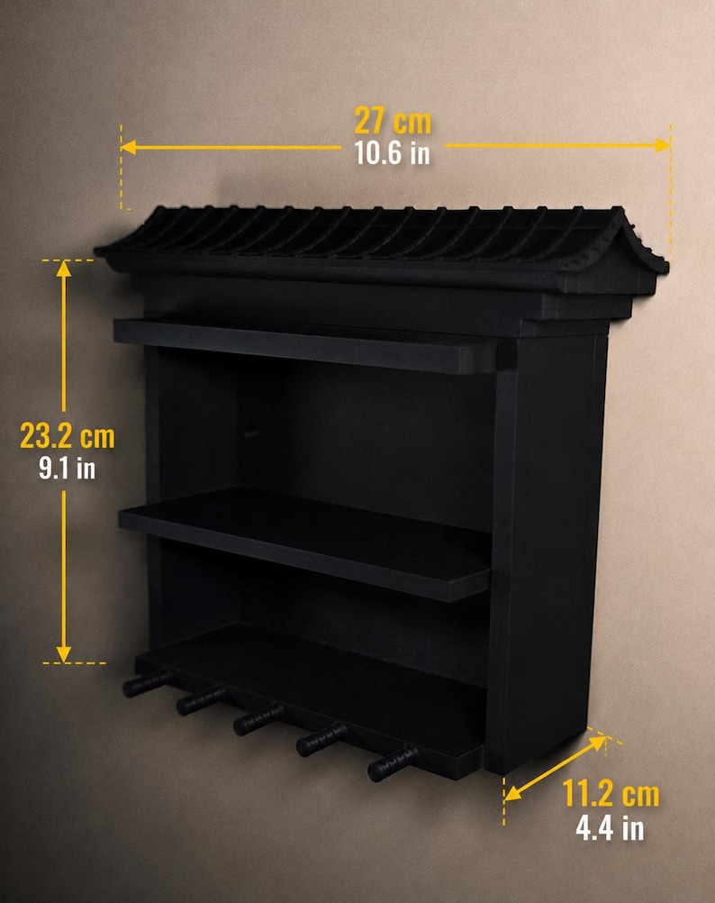 Peut inclure: Une &eacute;tag&egrave;re murale noire &agrave; trois niveaux avec cinq crochets en bas. Le sommet pr&eacute;sente une structure en forme de toit. Les dimensions sont de 27 cm de largeur, 23,2 cm de hauteur et 11,2 cm de profondeur, indiqu&eacute;es par le texte jaune.