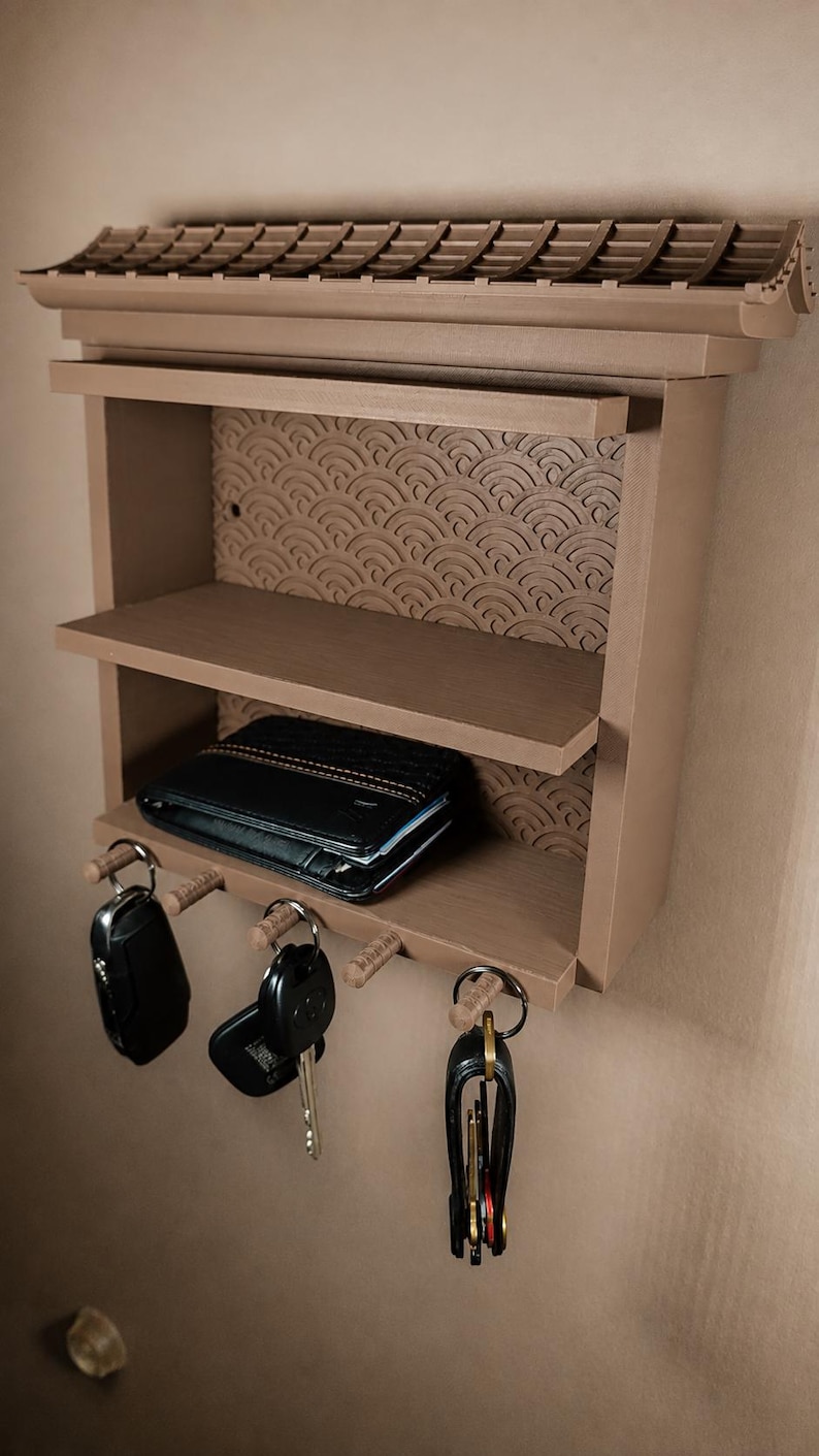 Peut inclure: Une &eacute;tag&egrave;re murale marron clair avec un sommet en forme de toit et un panneau arri&egrave;re textur&eacute; pr&eacute;sentant un motif de vagues r&eacute;p&eacute;titif. L'unit&eacute; comprend deux &eacute;tag&egrave;res horizontales et trois crochets en bois en bas, portant trois trousseaux de cl&eacute;s.