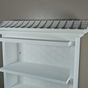 Peut inclure: Une &eacute;tag&egrave;re murale blanche dot&eacute;e d'une structure sup&eacute;rieure en forme de toit avec un motif de tuiles. Le panneau arri&egrave;re pr&eacute;sente un motif de vagues en relief r&eacute;p&eacute;titif. L'unit&eacute; comprend deux &eacute;tag&egrave;res horizontales et un cadre blanc mat.