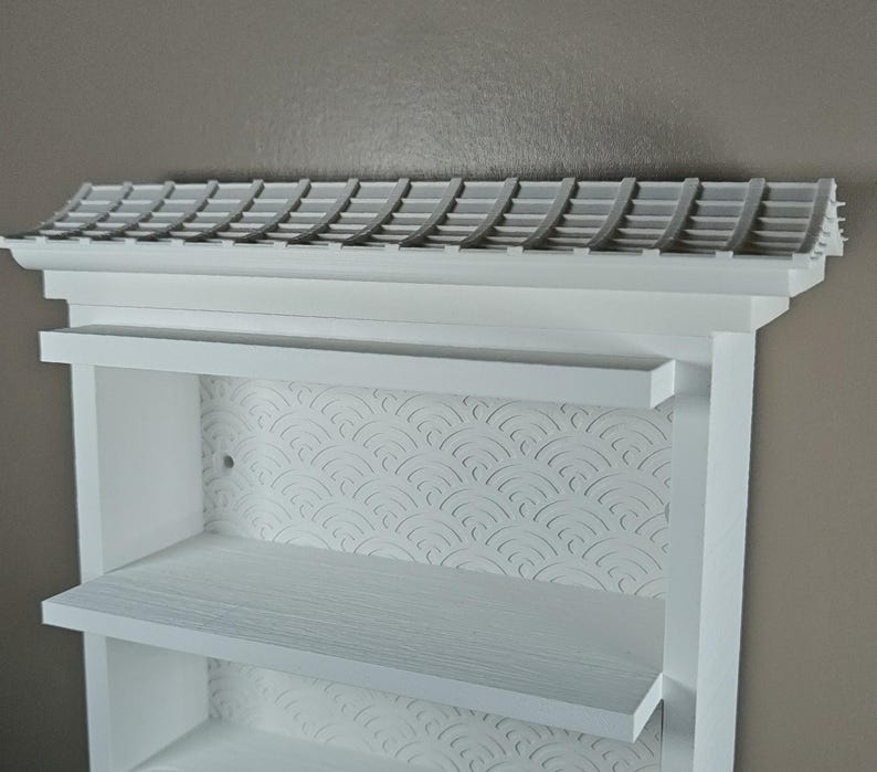 Peut inclure: Une &eacute;tag&egrave;re murale blanche dot&eacute;e d'une structure sup&eacute;rieure en forme de toit avec un motif de tuiles. Le panneau arri&egrave;re pr&eacute;sente un motif de vagues en relief r&eacute;p&eacute;titif. L'unit&eacute; comprend deux &eacute;tag&egrave;res horizontales et un cadre blanc mat.
