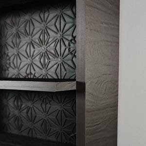 Peut inclure: Une &eacute;tag&egrave;re murale marron fonc&eacute; avec une finition en grain de bois textur&eacute; sur le cadre ext&eacute;rieur. Les panneaux arri&egrave;re des deux &eacute;tag&egrave;res visibles sont d&eacute;cor&eacute;s d'un motif g&eacute;om&eacute;trique en &eacute;toile r&eacute;p&eacute;titif dans une finition gris mat.