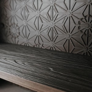 Peut inclure: Une &eacute;tag&egrave;re marron fonc&eacute; avec une texture de grain de bois, dot&eacute;e d'un panneau arri&egrave;re orn&eacute; d'un motif g&eacute;om&eacute;trique de triangles et de cercles r&eacute;p&eacute;t&eacute;s. L'&eacute;tag&egrave;re pr&eacute;sente une surface horizontale et une paroi arri&egrave;re verticale structur&eacute;e.