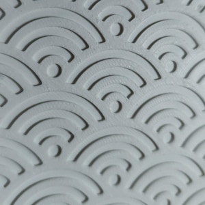 Peut inclure: Une surface blanche pr&eacute;sentant un motif en relief compos&eacute; de demi-cercles concentriques r&eacute;p&eacute;t&eacute;s en rang&eacute;es superpos&eacute;es. Le design cr&eacute;e un effet textur&eacute; en trois dimensions avec des ombres projet&eacute;es dans les rainures courbes du mat&eacute;riau blanc.
