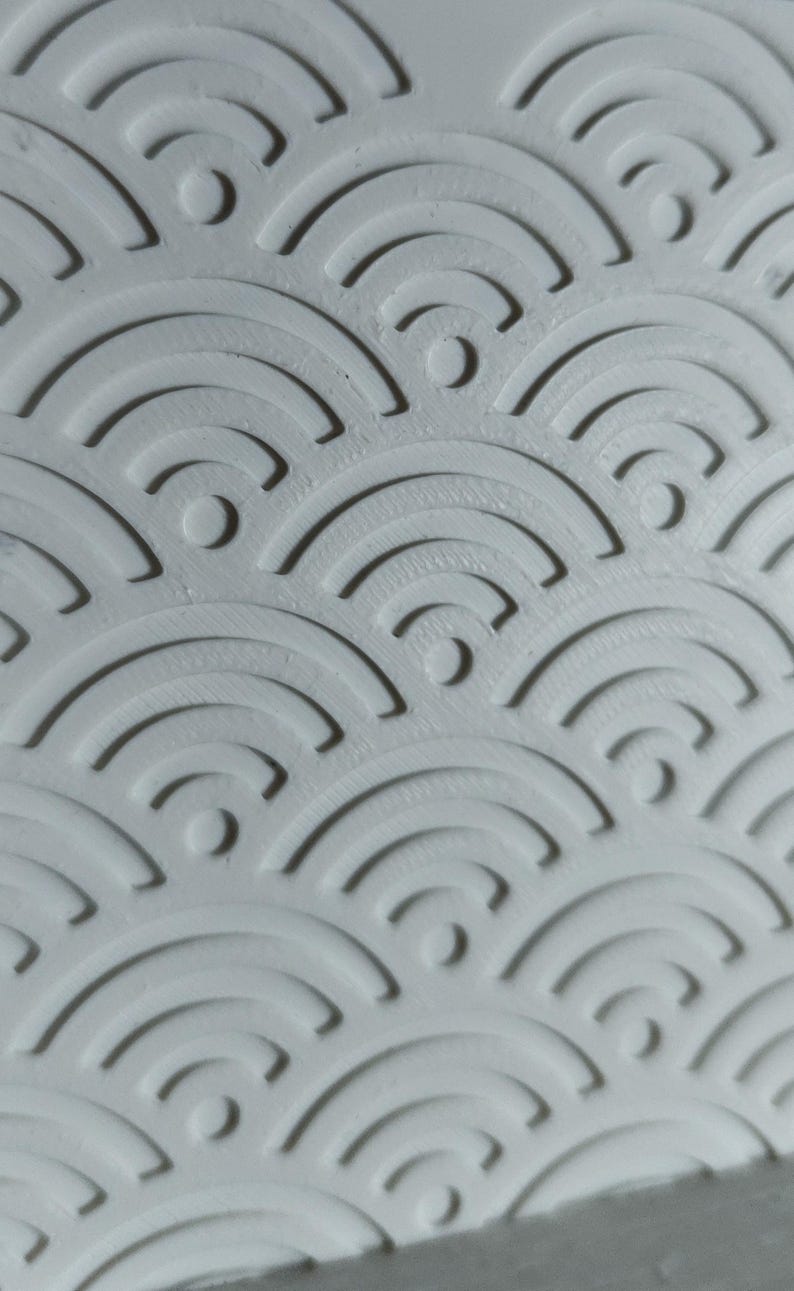 Peut inclure: Une surface blanche pr&eacute;sentant un motif en relief compos&eacute; de demi-cercles concentriques r&eacute;p&eacute;t&eacute;s en rang&eacute;es superpos&eacute;es. Le design cr&eacute;e un effet textur&eacute; en trois dimensions avec des ombres projet&eacute;es dans les rainures courbes du mat&eacute;riau blanc.