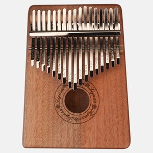 Puede incluir: Un kalimba de madera con 17 teclas de metal, cada una etiquetada con una nota musical. El kalimba es marr&oacute;n y tiene un agujero de sonido circular en el centro. El texto "Liyuan" est&aacute; grabado en la parte delantera del kalimba.