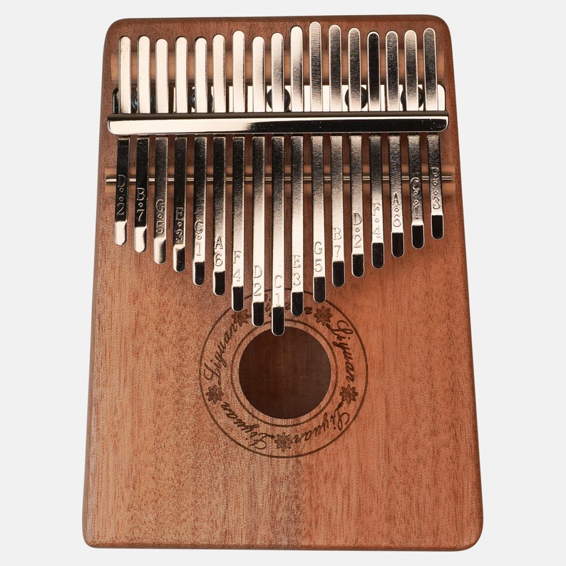 Puede incluir: Un kalimba de madera con 17 teclas de metal, cada una etiquetada con una nota musical. El kalimba es marr&oacute;n y tiene un agujero de sonido circular en el centro. El texto "Liyuan" est&aacute; grabado en la parte delantera del kalimba.