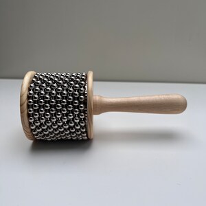 May include: A wooden shakers with a handle and a cylinder covered in silver metal beads.