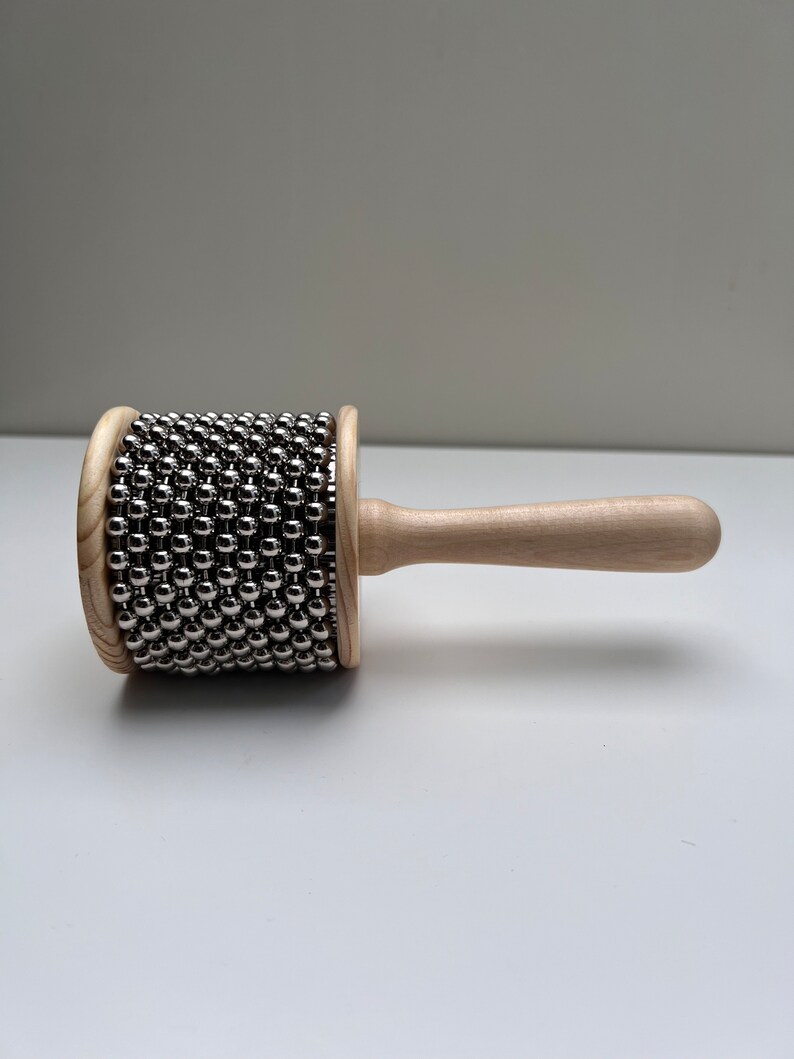May include: A wooden shakers with a handle and a cylinder covered in silver metal beads.