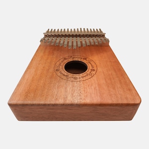 Puede incluir: Un kalimba de madera con un agujero de sonido circular y el texto "Lyrebird Lyrebird" grabado alrededor. El kalimba tiene 17 leng&uuml;etas met&aacute;licas.